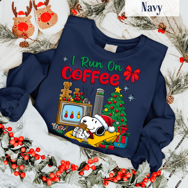 Adorable Snoopy holding a coffee cup with text 'I Run on Coffee and Christmas Cheer' on a holiday-themed T-shirt